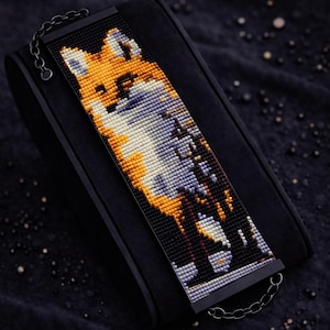 Könnte beinhalten: Ein Perlenarmbandmuster mit einem Fuchsmotiv in Orange, Weiß und Grau. Das Armband wird mit Miyuki Delica-Perlen hergestellt und ist an einer schwarzen Metallkette befestigt. Der Text "Bracelet Bead Pattern" und "LOOM STITCH" sind sichtbar.