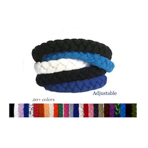 May include: A stack of five braided fabric headbands in black, blue, white, black, and blue. Below the stack, a horizontal strip displays twenty-plus different color options for the adjustable headbands, including shades of red, orange, green, and purple.