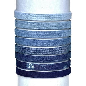 May include: A stack of eight denim headbands in various shades of blue, from light to dark. The headbands are made of denim fabric and have a simple design.