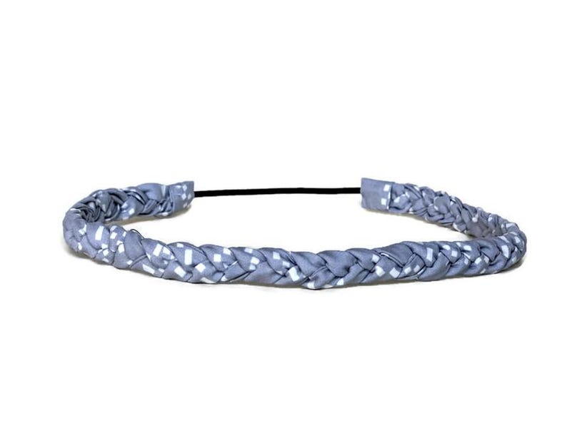 May include: A braided headband featuring a light blue fabric with a repeating white square pattern. The braided section is connected by a thin, black elastic band at the back, creating a circular shape for the hair accessory.