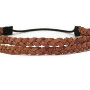 May include: A brown braided leather headband with a black elastic band. The headband features two rows of braided leather and is designed for comfortable wear. This accessory is suitable for various hairstyles.