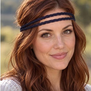 May include: A double-strand navy blue braided headband worn across the forehead. The accessory features two thin, woven fabric cords that wrap around the head, providing a simple and secure fit for various hair styles and lengths.