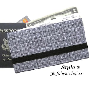 May include: A gray and black passport holder with a black elastic band. The holder is made of a textured fabric and has the text "Style 2" and "36 fabric choices" printed on it.