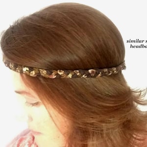 May include: A braided headband featuring a mix of dark brown, tan, and metallic gold tones. The headband is worn around the head, and the text "similar sized headband" is printed in black on the right side of the image.