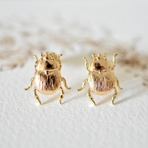 Peut inclure: Une paire de boucles d'oreilles en forme de scarabée dorées. Les boucles d'oreilles sont petites et délicates, et présentent un design de scarabée réaliste.