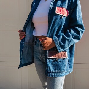 May include: A blue denim jacket with a zipper closure and two large patch pockets. The pockets have brown and pink fabric accents.