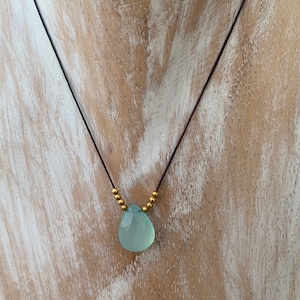 Peut inclure: Un collier délicat avec un pendentif en forme de larme de pierre précieuse bleu clair et des perles dorées.