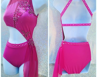 May include: A pink dance leotard with a halter neckline and a sheer pink overlay. The leotard is decorated with rhinestones and has a cutout on the side. The back of the leotard has a criss-cross strap design.