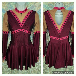 May include: A burgundy figure skating dress with long sleeves, a pink and black trim, and a sheer nude overlay. The dress is decorated with rhinestones.