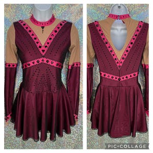 May include: A burgundy figure skating dress with long sleeves, a pink and black trim, and a black mesh overlay. The dress has a scoop neckline and a keyhole back.