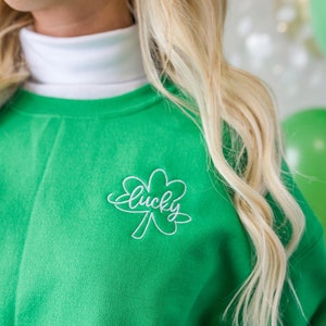 May include: Green sweatshirt with a white embroidered four-leaf clover and the word "lucky" on the front.