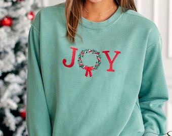 May include: A teal green sweatshirt with a red embroidered wreath and the word "JOY" on the front.