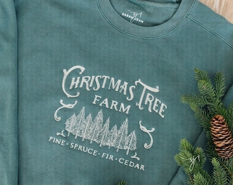 Może przedstawiać: Turkusowa bluza z białym haftem, na którym widnieje napis "Christmas Tree Farm" wraz z rysunkiem sosen i tekstem "Pine, Spruce, Fir, Cedar".