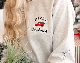 May include: Gray sweatshirt with the text "Merry Christmas" and a red truck carrying a green Christmas tree. The sweatshirt has a small signature on the sleeve.