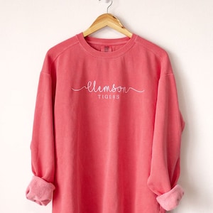 May include: A coral coloured sweatshirt with the words "Clemson Tigers" embroidered in white on the front.