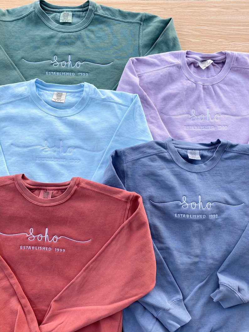 May include: Five different coloured sweatshirts with the text "Soho Established 1999" embroidered on the front in white. The sweatshirts are in the colours green, purple, light blue, blue, and red.