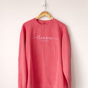 May include: A coral pink sweatshirt with a white cursive "clemson tigers" logo.
