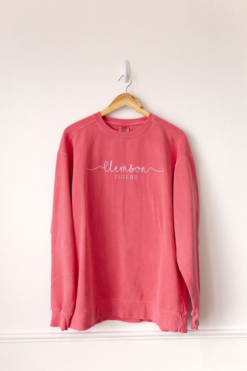 May include: A coral pink sweatshirt with a white cursive "clemson tigers" logo.
