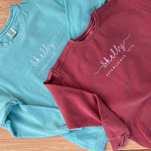 May include: Two sweatshirts, one teal blue and one maroon, with the text "Shelly Established 1910" embroidered on the front.