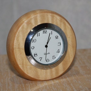 May include: A round wooden clock with a white face and black numbers. The clock has a silver trim and says "Quartz" on the face.