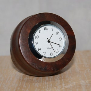 May include: A round, wooden clock with a white face and black hands. The clock has a silver rim and the word "Quartz" printed on the face.