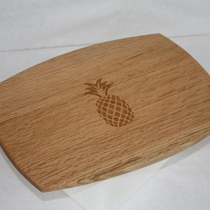 Könnte beinhalten: Ein Holz-Servierbrett mit einem geschnitzten Ananas-Design. Das Brett ist hellbraun und hat eine natürliche Holzmaserung.