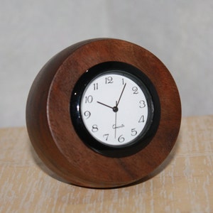 May include: A round wooden clock with a black face and white numbers. The clock is made of dark wood and has a black rim around the face.