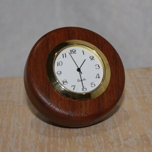 May include: A round wooden clock with a gold rim and white face. The clock has black hands and black numbers.
