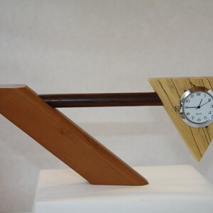 May include: A wooden clock with a triangular base and a silver face. The clock is made of different types of wood, including a dark brown wood and a light brown wood.