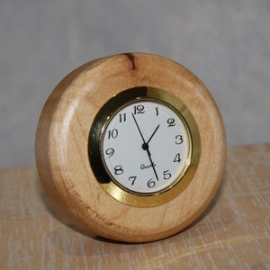 May include: A round wooden clock with a gold rim and white face. The clock face has black numbers and hands. The clock says "Quartz" at the bottom.