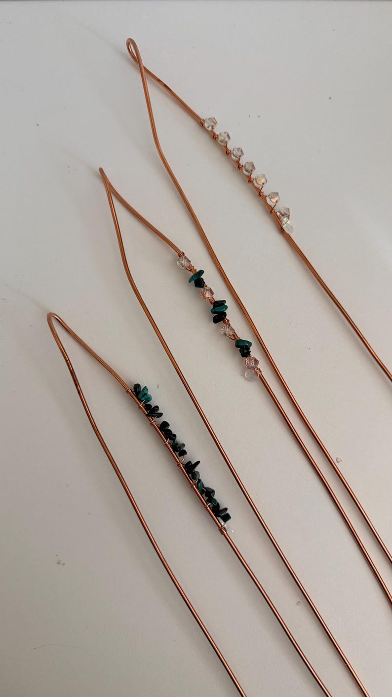 May include: Four copper hair pins with decorative bead accents. Each pin features a different arrangement of beads, including clear crystals, pink beads, and dark green stones. The pins are arranged diagonally against a white background.