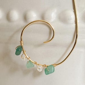May include: A gold-colored metal spiral-shaped bookmark. The bookmark is adorned with small, polished green and clear gemstones. The gemstones are wire-wrapped onto the spiral, adding a touch of elegance to this unique accessory.