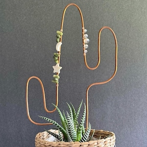 May include: Copper wire cactus plant holder with green and white beads and a succulent plant in a woven basket.