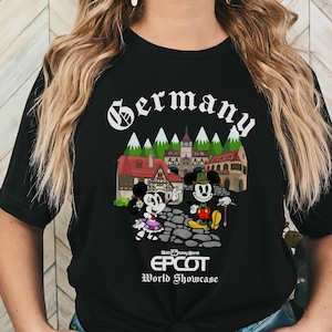 May include: Black t-shirt with a white graphic of Mickey and Minnie Mouse in German attire in front of a German village. The text "Germany" is at the top of the graphic and "Walt Disney World EPCOT World Showcase" is at the bottom.