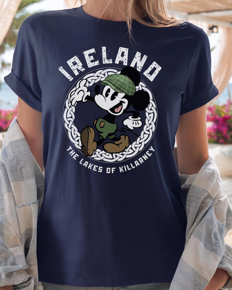 Puede incluir: Camiseta azul marino con Mickey Mouse de dibujos animados con gorro y pantalones cortos a cuadros verdes, con el texto "IRELAND" y "THE LAKES OF KILLARNEY" en un dise&ntilde;o circular blanco. La camiseta tiene mangas enrolladas.