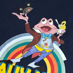May include: Navy blue t-shirt with a cartoon frog character holding a Mickey Mouse-shaped object and ice cream. The frog wears a suit and bow tie, with a Mickey Mouse shirt. The shirt has the text "ALLY HO!" in yellow, above a rainbow.