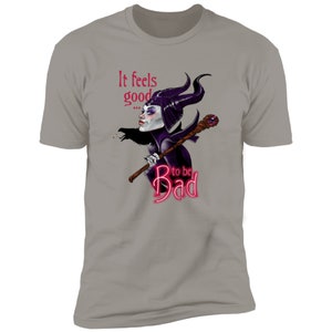 Puede incluir: Una camiseta gris jaspeada con una ilustraci&oacute;n morada y negra de Mal&eacute;fica de La Bella Durmiente de Disney. El texto "It feels good... to be Bad" est&aacute; impreso en rosa en la camiseta.
