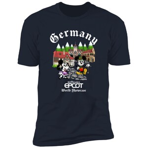 May include: A navy blue t-shirt with a white graphic of Mickey and Minnie Mouse in front of a German village. The text "Germany" is above the graphic and "Walt Disney World EPCOT World Showcase" is below the graphic.