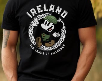 May include: Black t-shirt with a cartoon character in a green hat and outfit, encircled by a white Celtic knot design. The text "IRELAND" and "THE LAKES OF KILLARNEY" are printed in white, evoking Irish heritage.