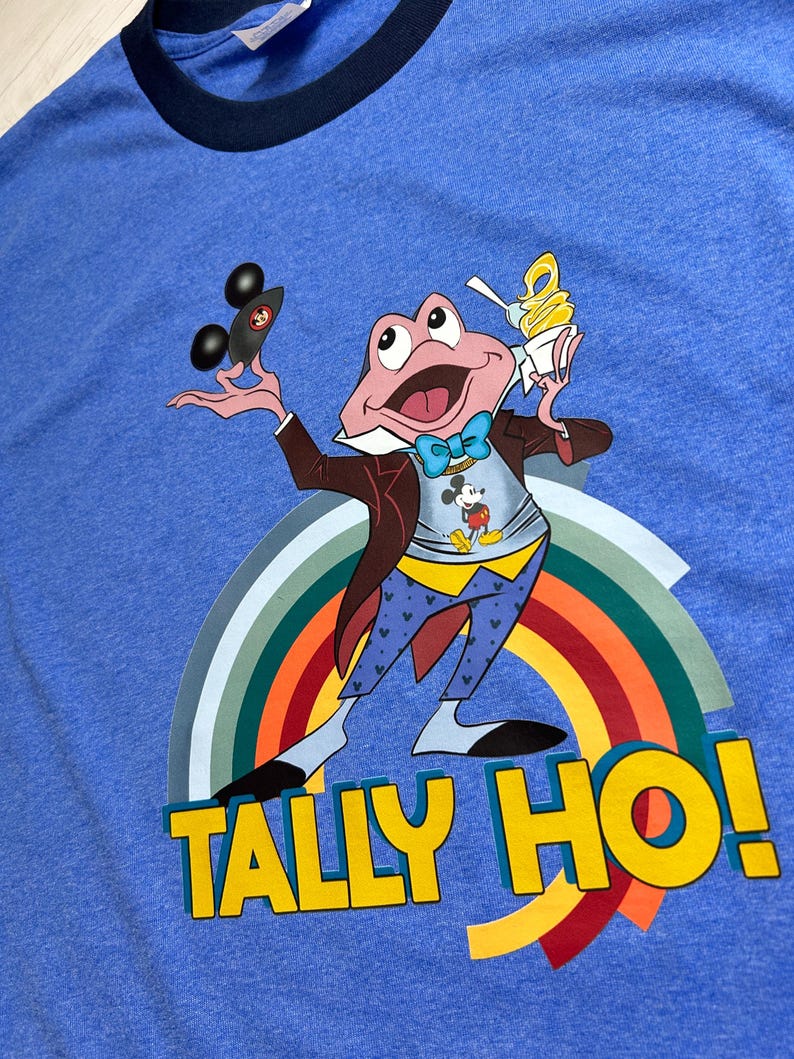 May include: Blue ringer t-shirt with a cartoon frog character wearing a bow tie, holding a black car and an ice cream cone. The frog is in front of a rainbow, with the words "TALLY HO!" in yellow.