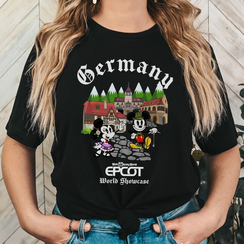 May include: Black t-shirt with a white graphic of Mickey and Minnie Mouse in German attire in front of a German village. The text "Germany" is at the top of the graphic and "Walt Disney World EPCOT World Showcase" is at the bottom.