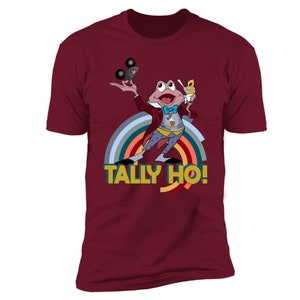 May include: Burgundy t-shirt with a cartoon frog in a red coat, holding a Mickey Mouse ice cream and a Mickey Mouse ear hat. The shirt has a rainbow design and the text "TALLY HO!"