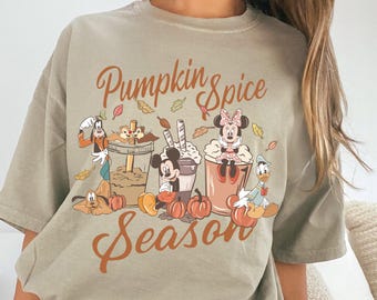 May include: A light olive green t-shirt with the words "Pumpkin Spice Season" in brown script. The shirt features cartoon characters like Mickey and Minnie Mouse, Goofy, and Donald Duck with fall-themed elements.