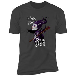Puede incluir: Una camiseta gris oscuro con un gr&aacute;fico blanco de una Mal&eacute;fica de dibujos animados de La Bella Durmiente de Disney. El gr&aacute;fico presenta a Mal&eacute;fica con sus cuernos, vestido morado y sosteniendo un bast&oacute;n. El texto "It feels good... to be Bad" est&aacute; impreso en blanco en la camiseta.