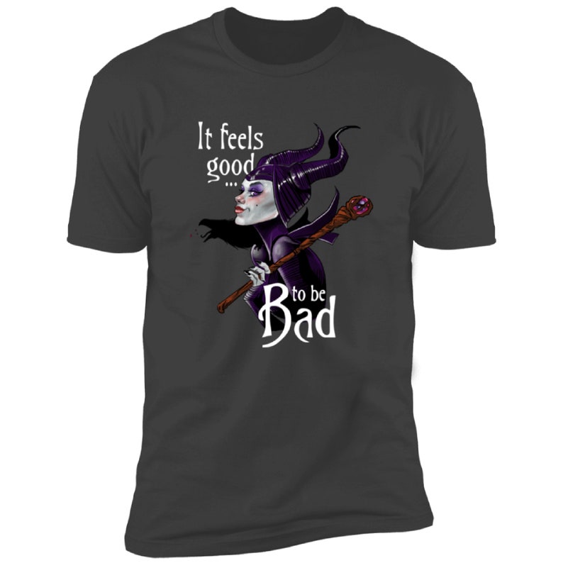 Puede incluir: Una camiseta gris oscuro con un gr&aacute;fico blanco de una Mal&eacute;fica de dibujos animados de La Bella Durmiente de Disney. El gr&aacute;fico presenta a Mal&eacute;fica con sus cuernos, vestido morado y sosteniendo un bast&oacute;n. El texto "It feels good... to be Bad" est&aacute; impreso en blanco en la camiseta.