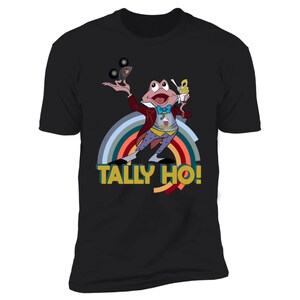 May include: Black t-shirt with a cartoon frog character in a red coat and bow tie, holding a dessert and juggling. The shirt has a rainbow design and the text "TALLY HO!" in yellow and blue.
