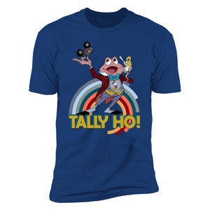 May include: A navy blue t-shirt with a cartoon frog juggling black Mickey Mouse-shaped objects and holding a sundae. The frog wears a red coat, a blue bow tie, and a vest with a Mickey Mouse design. The text "TALLY HO!" is below a rainbow.