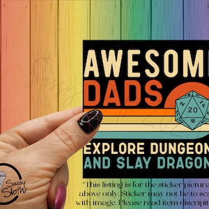 May include: Black square sticker with the text "AWESOME DADS EXPLORE DUNGEONS AND SLAY DRAGONS" in white and orange. The design includes a D20 die and a retro sunset background. The sticker is held by a hand.