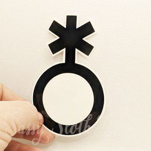 May include: Black and white gender symbol sticker with a starburst design. The symbol is a circle with a cross inside, representing the union of male and female.