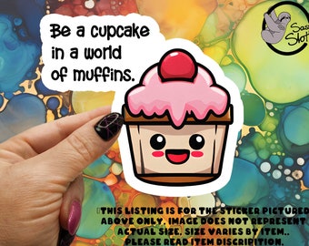 May include: A sticker with a cartoon cupcake with a pink frosting and a red cherry on top. The cupcake has a happy face and the text "Be a cupcake in a world of muffins." is written above it.